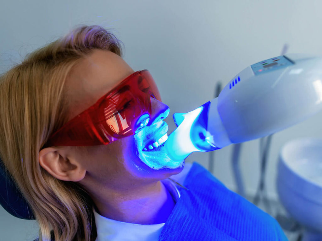 woman at the dentist getting a professional teeth whitening treatment, with a uv light shining on her teeth
