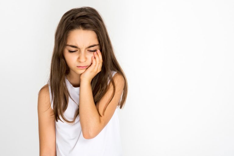 A young girl holds her jaw in the palm of her hand with a pained look on her face