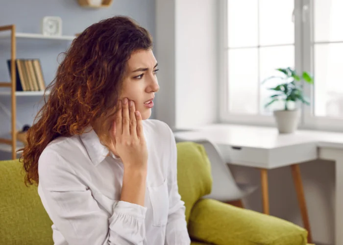 Stock image of a woman looking distressed, holding her jaw due to tooth pain.